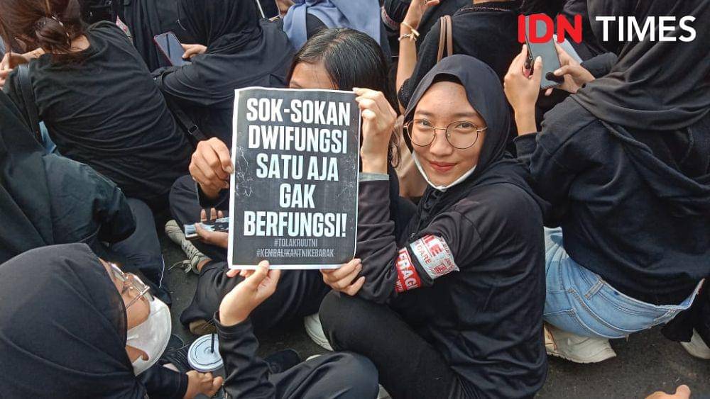 Seorang mahasiswi tersenyum dengan membawa spanduk menyindir pengesahan UU TNI. (IDN Times/Fariz Fardianto)