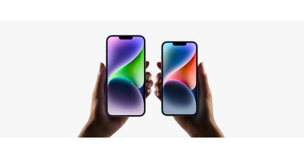 Dua tangan memegang iPhone 14 dan iPhone 14 Plus dengan layar menyala menampilkan warna gradasi cerah di latar putih.