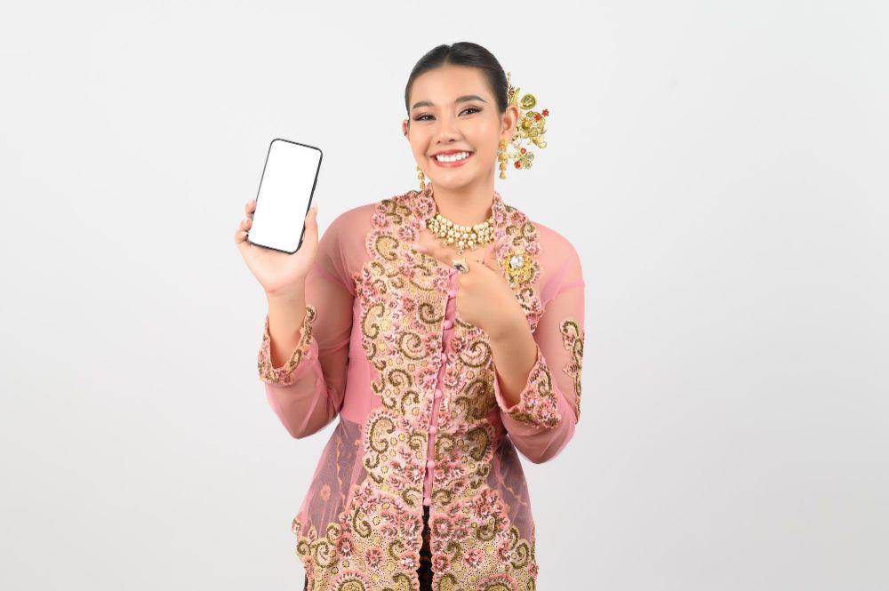 ilustrasi perempuan sedang mengenakan kebaya dan memegang smartphone (freepik.com/johnstocker)