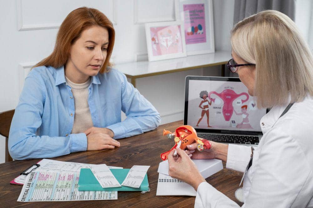Seorang perempuan berkonsultasi dengan dokter spesialis kandungan yang menjelaskan anatomi rahim menggunakan model organ reproduksi.