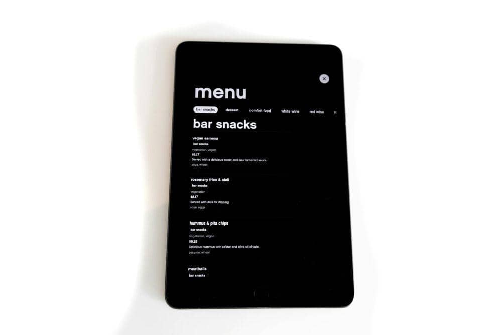 Tampilan layar tablet berwarna hitam menampilkan daftar menu makanan bar snacks dengan beberapa pilihan hidangan dan harga.