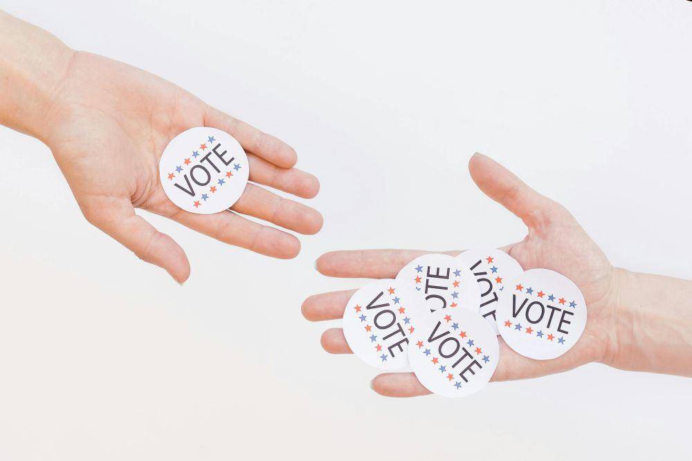 Ilustrasi dua tangan yang saling berhadapan dengan stiker bertuliskan "VOTE" (Pexels.com/Mikhail Nilov)