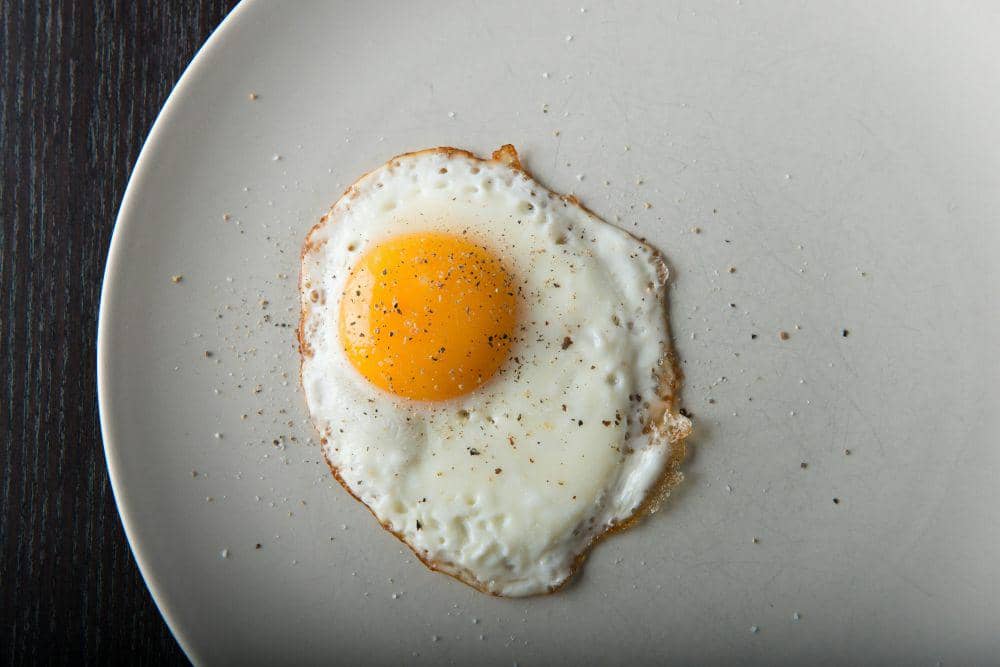 a fried eeg on a white plate on a wooden table(https://unsplash.com/photos/a-fried-egg-on-a-white-plate-on-a-wooden-table-pvbKrbqN54g)
