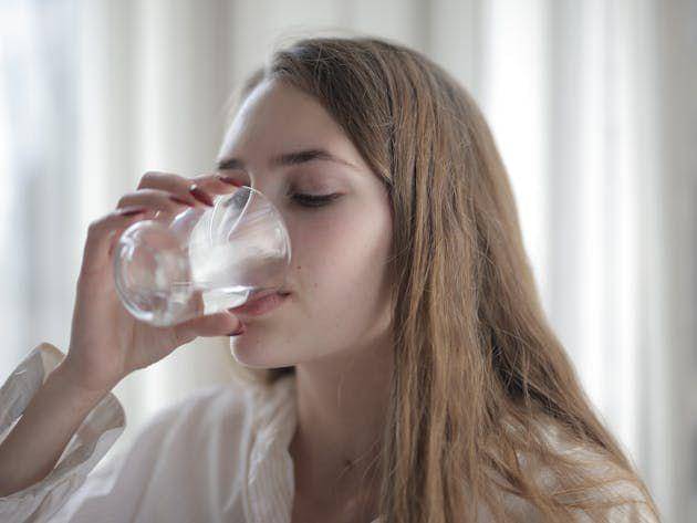 Seorang perempuan minum segelas air putih.