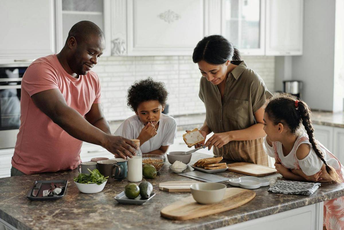 Ayah, ibu, dan dua anak perempuannya sedang bersama-sama menyiapkan makanan di dapur.