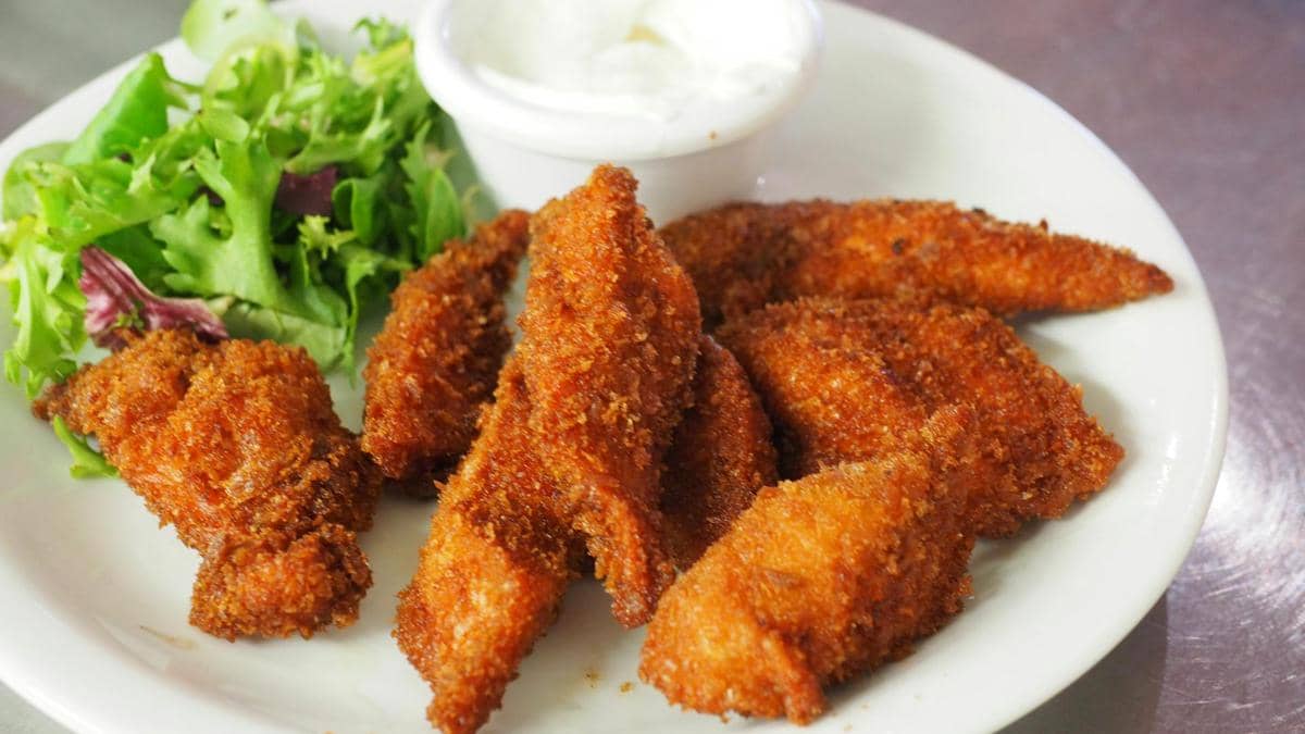 Beberapa potong chicken wings goreng berbalut tepung renyah disajikan di piring putih bersama salad hijau dan saus celup.