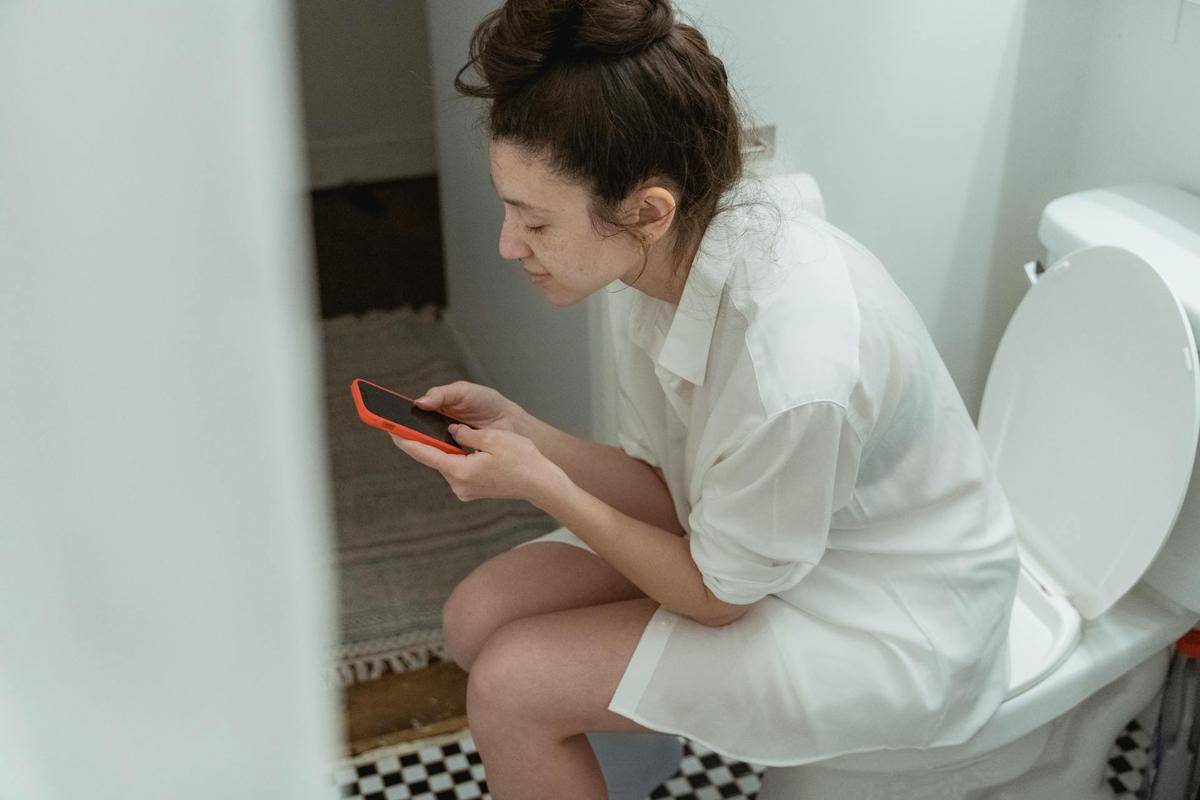 ilustrasi menggunakan gadget di toilet