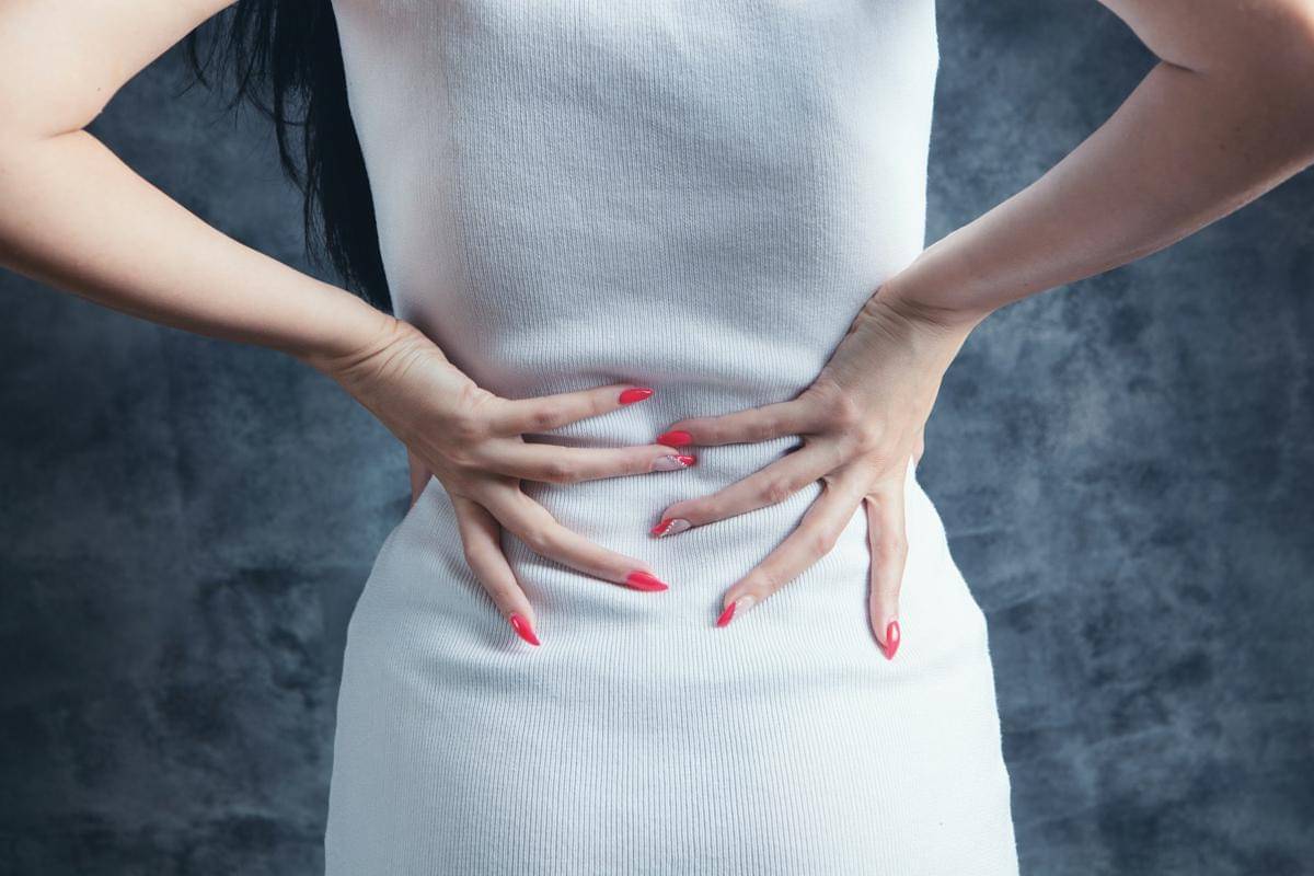 Seorang perempuan memegang bagian belakang pinggang dengan kedua tangannya.