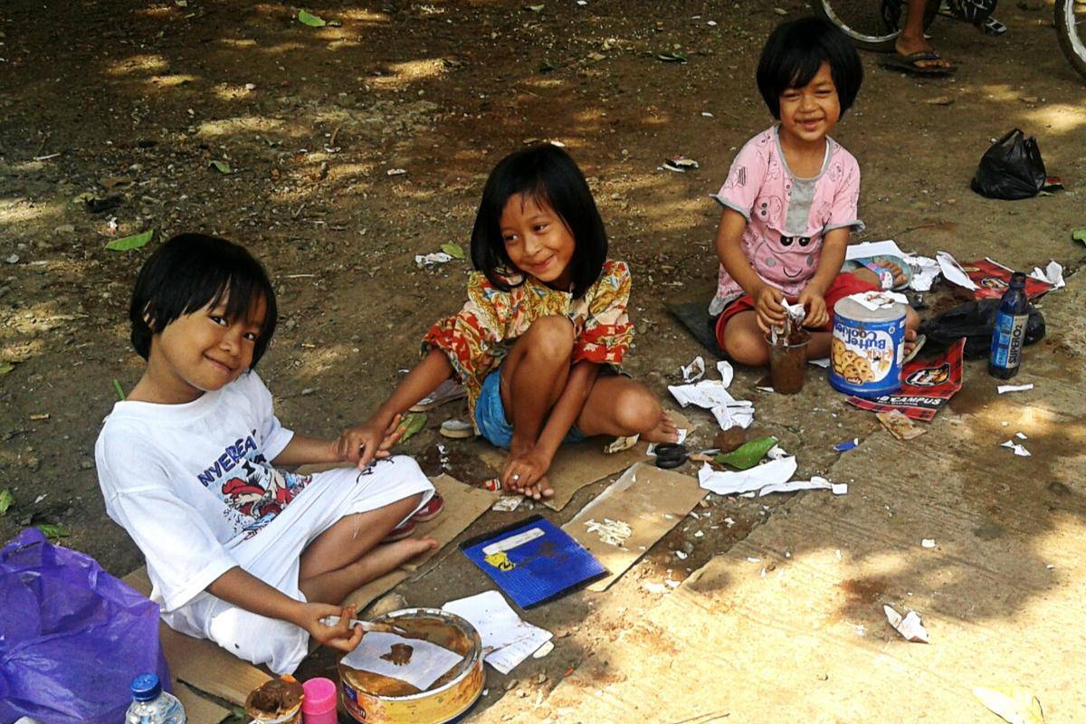 Anak-anak menikmati permainan tradisional jual-jualan di bawah pohon rindang. Dengan peralatan sederhana dari barang bekas, mereka berperan sebagai penjual dan pembeli sambil berkreasi dengan pasir, daun, dan kertas bekas. Sumber gambar: tablemat.wordpress.com