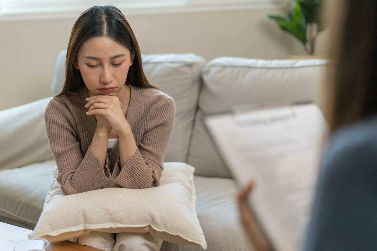 Seorang perempuan duduk di sofa, tampak merenung, dalam sesi konsultasi dengan tenaga medis.