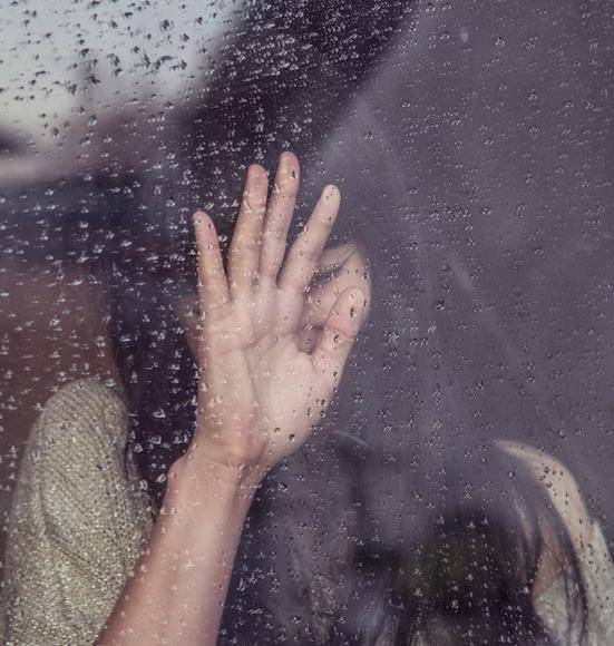 Foto wanita menyentuh kaca ketika hujan. [UNSPLASH]