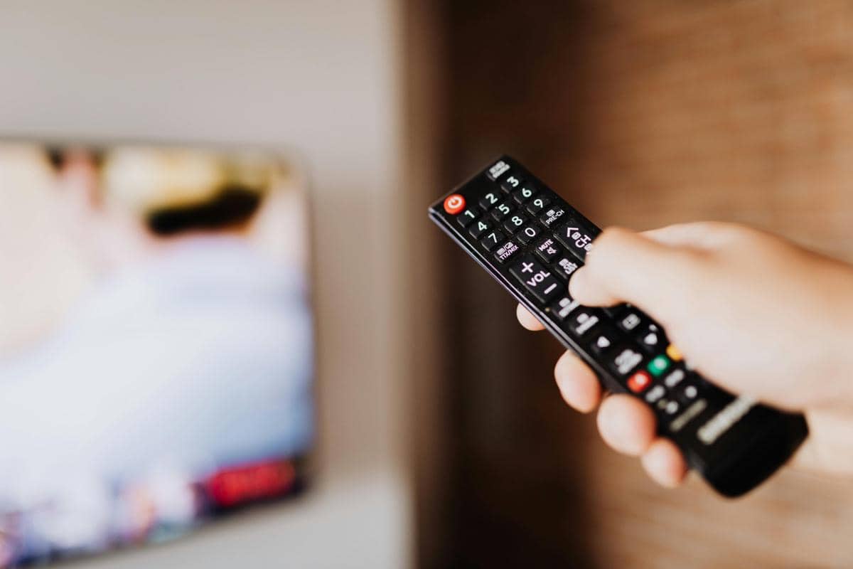 Orang memegang remote untuk menonton televisi