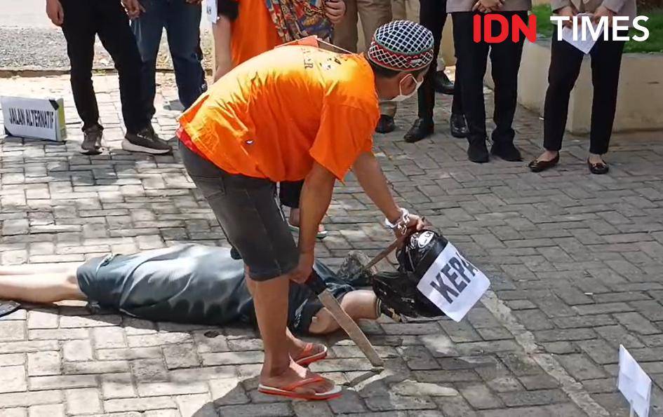 Adegan saat tersangka P usai menebas kepala korban D dan mengangkatnya kemudian dibuang, dalam rekonstruksi kasus suami dimutilasi kakak beradik yang terjadi di Desa Paramasan Atas, Banjar, Kalsel. Reka adegan ulang berlangsung di halaman Satreskrim Polrers Banjar, di Martapura, Kamis (7/8/2025). (Hendra Lianor/IDN Times)