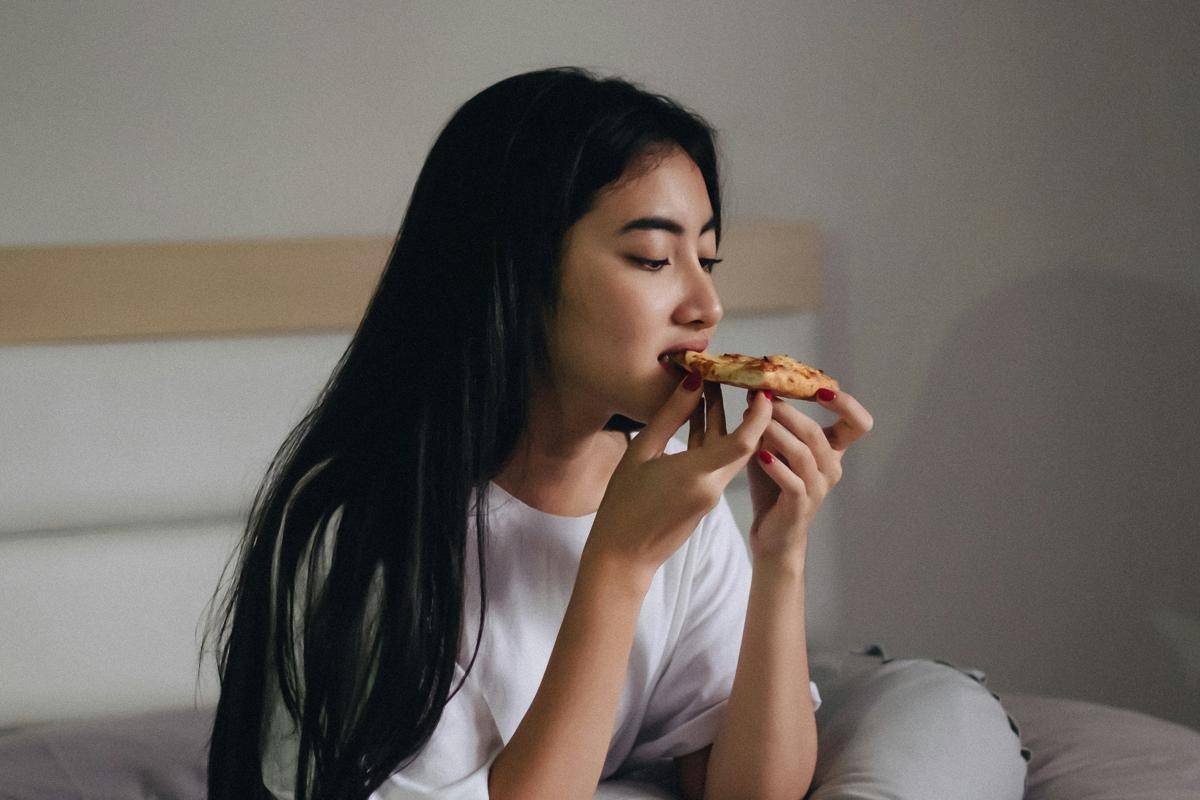 ilustrasi seorang wanita muda sedang memakan makanan di atas tempat tidur (unsplash.com/henru wicaksono)