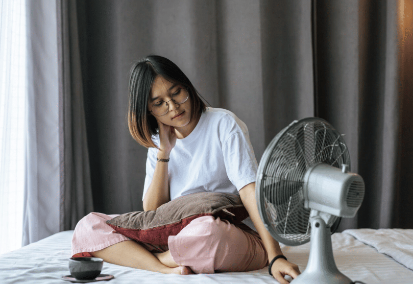 Seorang perempuan menyejukkan diri di depan kipas angin saat cuaca panas.