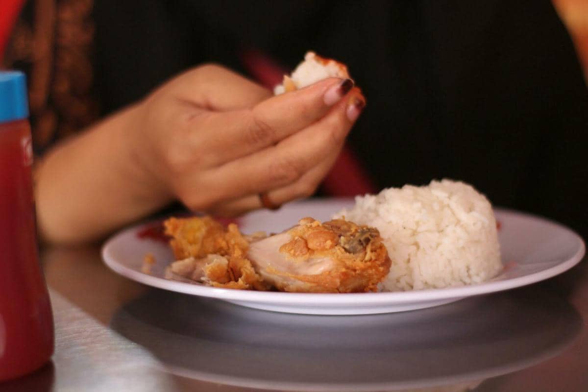 Ilustrasi sepiring nasi putih dengan potongan ayam goreng renyah yang disantap langsung menggunakan tangan.