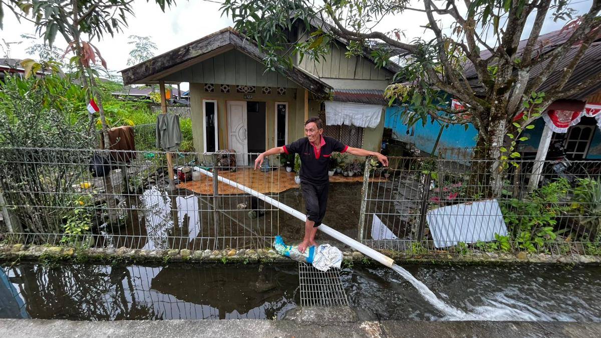 Warga Jalan Anggrek, Suardi, berdiri depan rumahnya yang terendam banjir. Ia berupaya menguras banjir menggunakan mesin alkon. (IDN Times/Endy Langobelen)