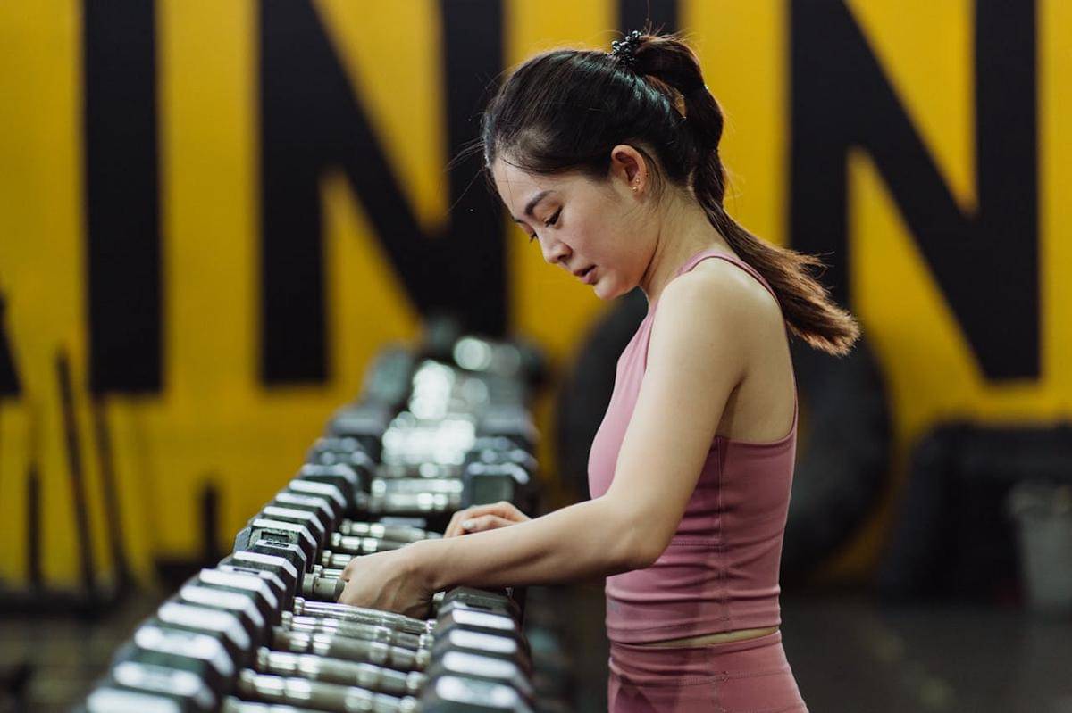 Seorang perempuan latihan beban di gym dengan dumbel.