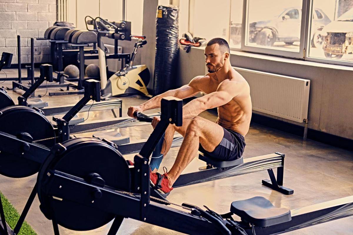 Seorang pria melakukan latihan dengan rowing machine di gym.