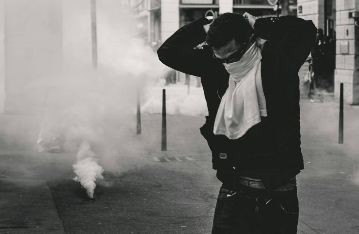gambar seorang pendemo berusaha melindungi diri dari paparan gas air mata (unsplash.com/ev)