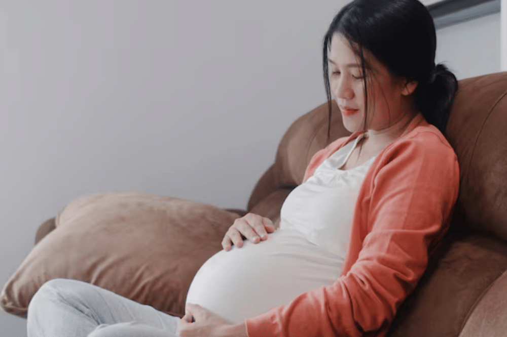 Ilustrasi ibu hamil duduk di sofa, memegangi perutnya.