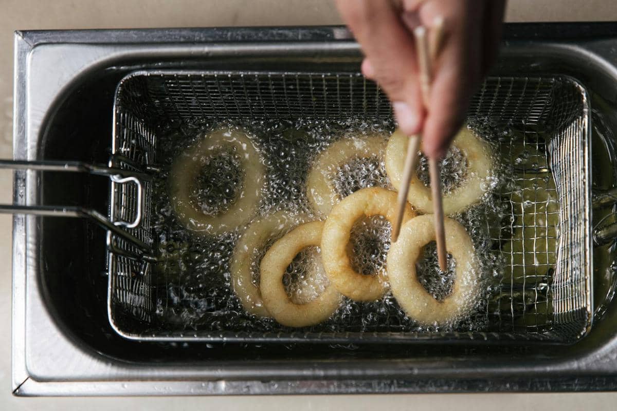 Tangan memegang wajan di atas kompor sambil menggoreng makanan dalam minyak panas di dapur rumah.