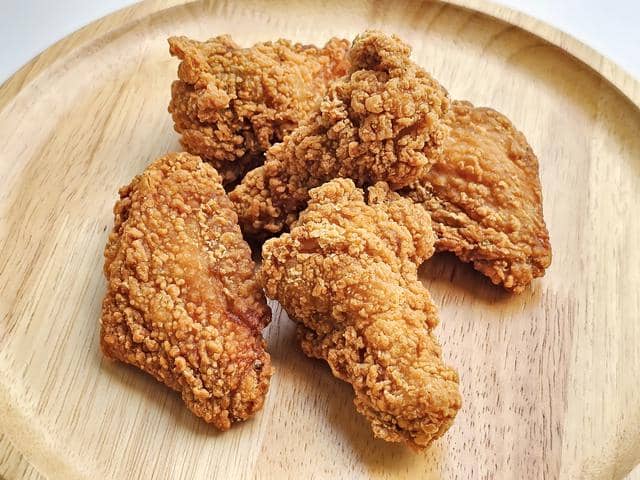 Beberapa potong ayam goreng crispy berwarna keemasan tersaji di atas piring kayu bundar dengan tekstur renyah menggugah selera.