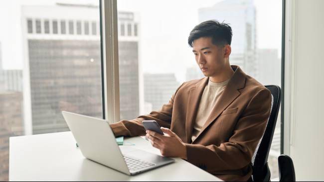 Ilustrasi pria profesional bekerja di kantor modern, memanfaatkan laptop dan ponsel untuk menunjang produktivitas (Sumber: Dok. Envato)