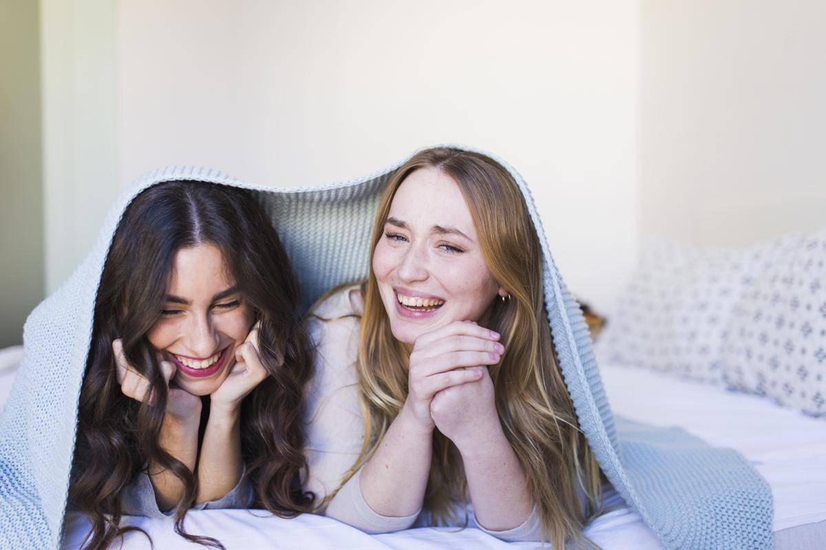 Dua perempuan sedang tertawa bersama di bawah selimut (freepik.com)