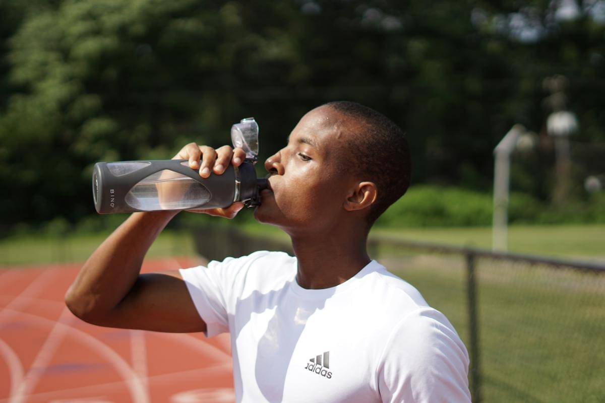 Seorang laki-laki minum air putih dari botol minum saat rehat olahraga.