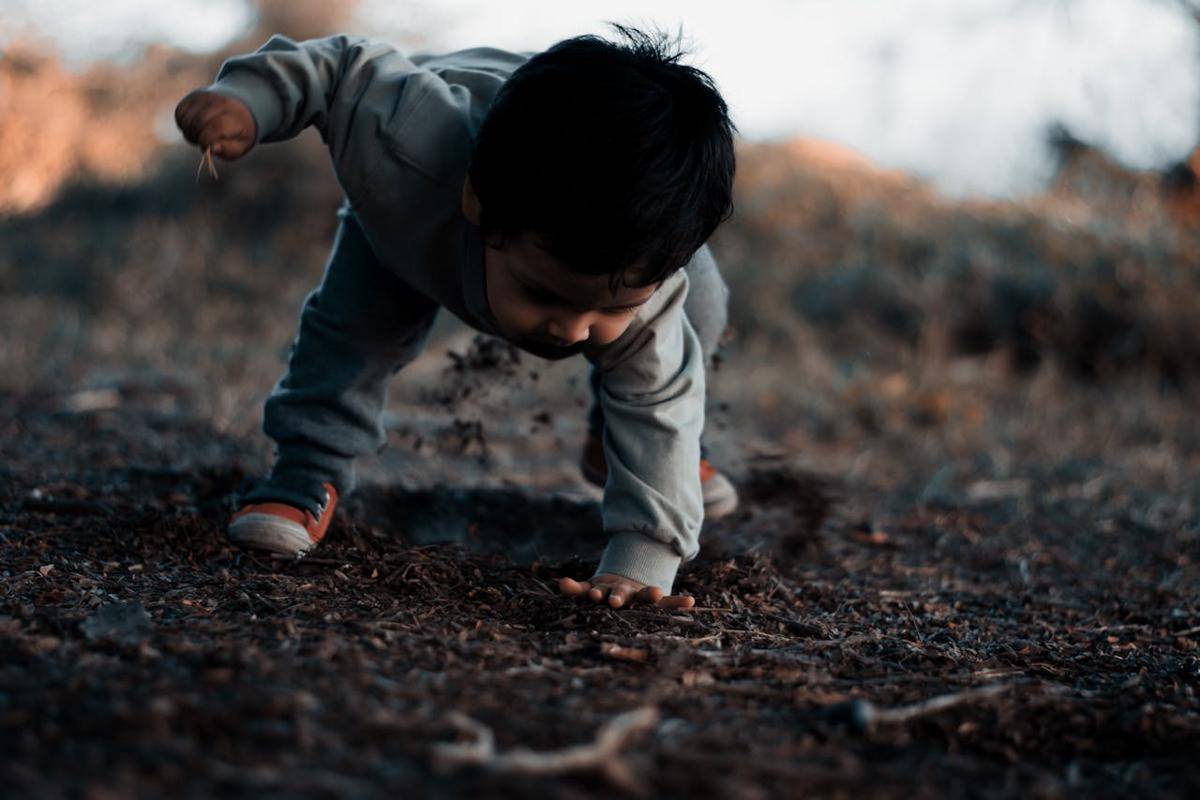 Seorang anak kecil memegang tanah berwarna hitam dengan satu tangannya.