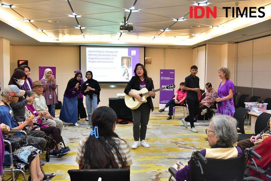 Seorang terapis musik bermain gitar di tengah audiens dan pasien demensia.