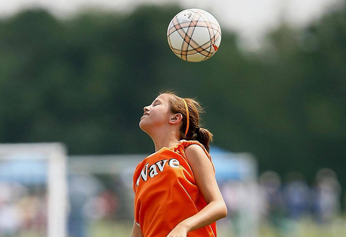 Seorang remaja putri menyundul bola dalam permainan sepak bola.
