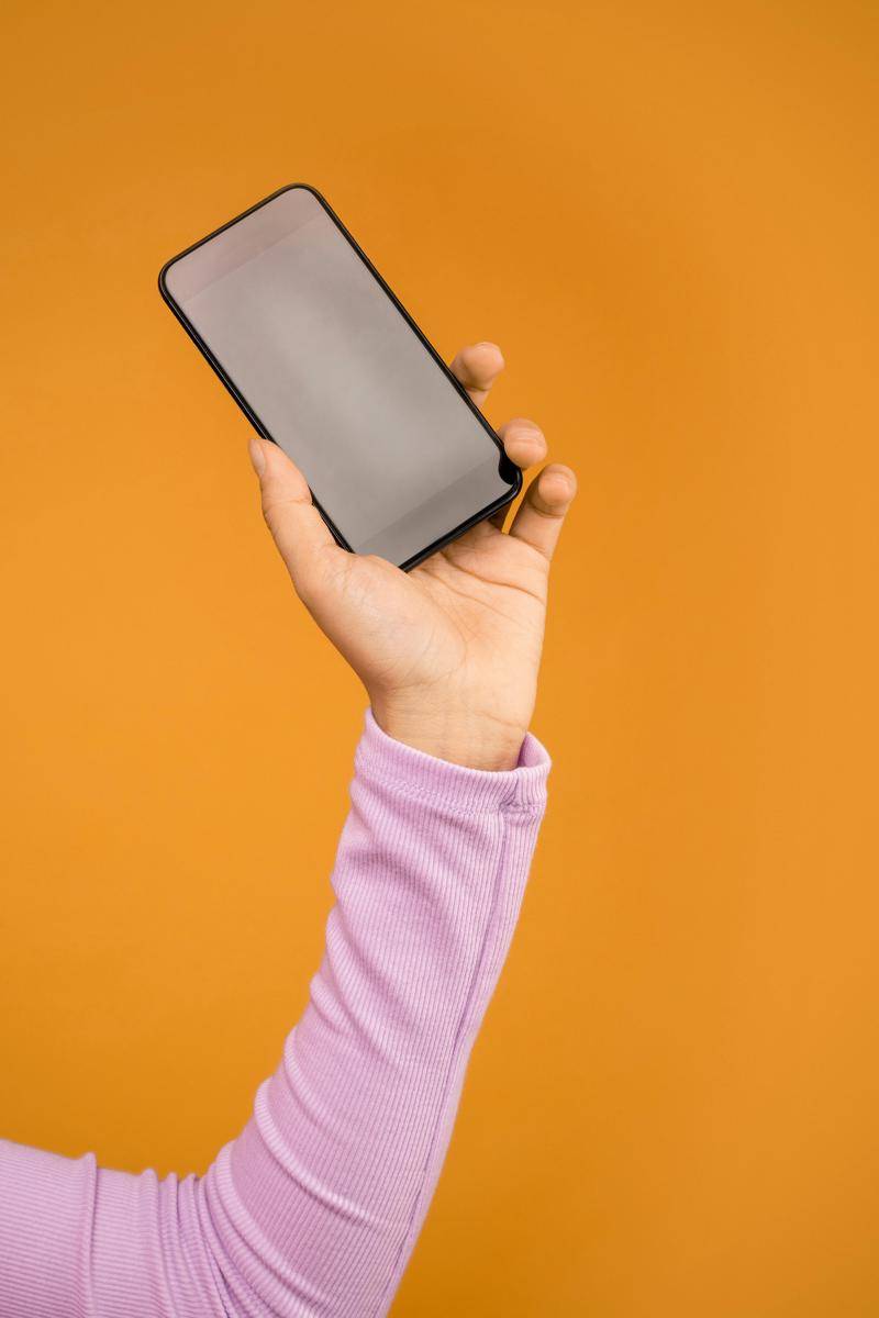 ilustrasi orang yang memegang smartphone hitam dengan latar belakang oranye (pexels.com/Sound On)