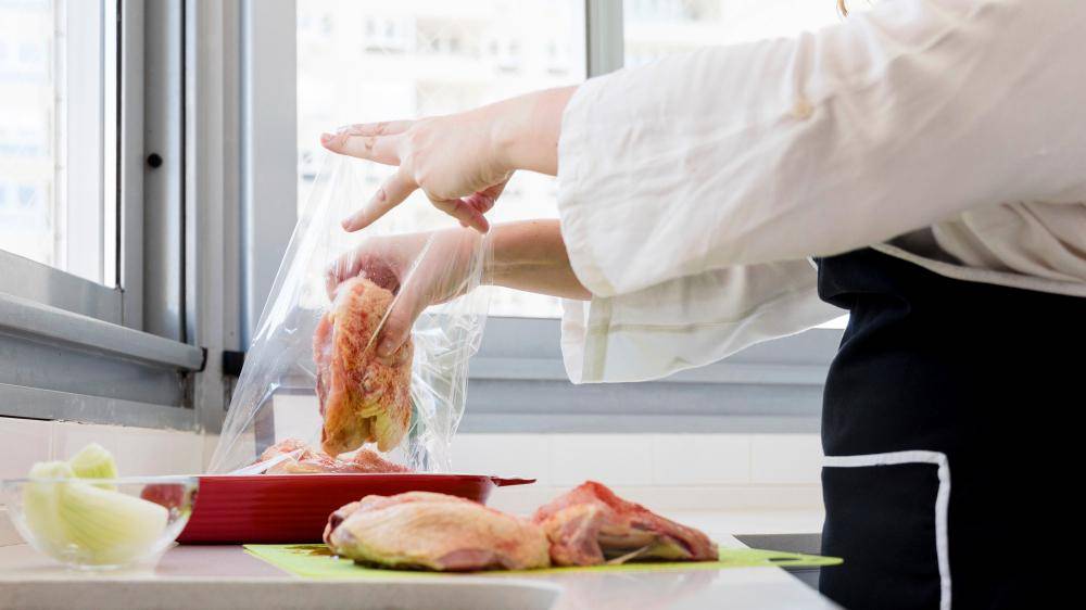 Seseorang sedang memasukkan daging ayam mentah ke dalam plastik di dapur.