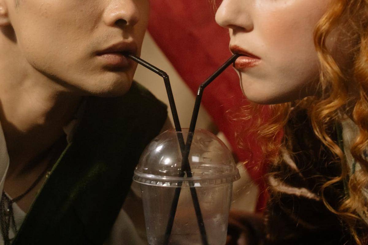 Perempuan dan laki-laki minum pakai sedotan dari gelas yang sama.