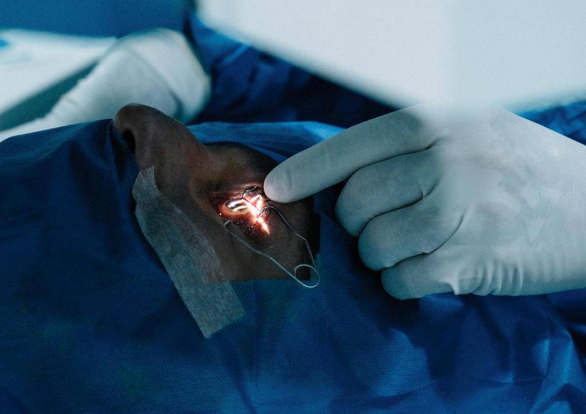 Seorang dokter memegangi dan menerangi mata pasien yang sedang berbaring.