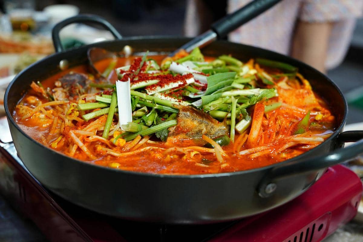 Semangkuk kimchi jjigae berkuah merah dengan potongan kimchi dan tahu sebagai ilustrasi hidangan Korea.