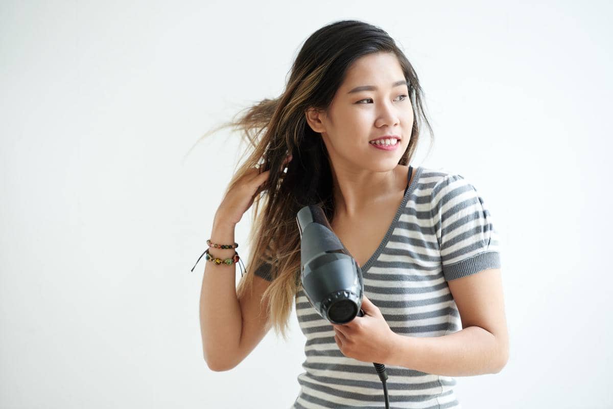 Seorang perempuan menggunakan hair dryer atau pengering rambut.