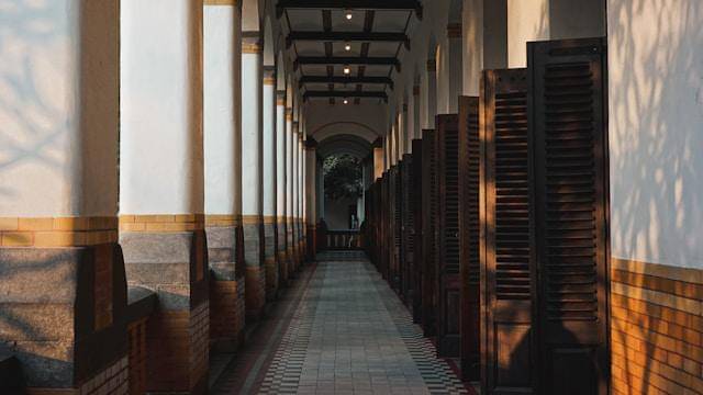 A long hallway lined with wooden doors and windows (unsplash.com/@triadiyusuf)