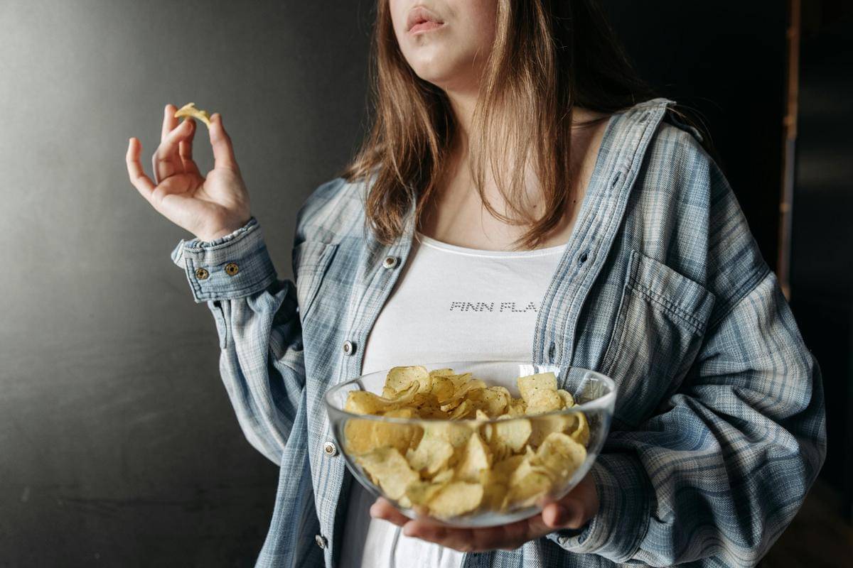 Seorang perempuan mengonsumsi keripik kentang, salah satu jenis makanan ultra proses.