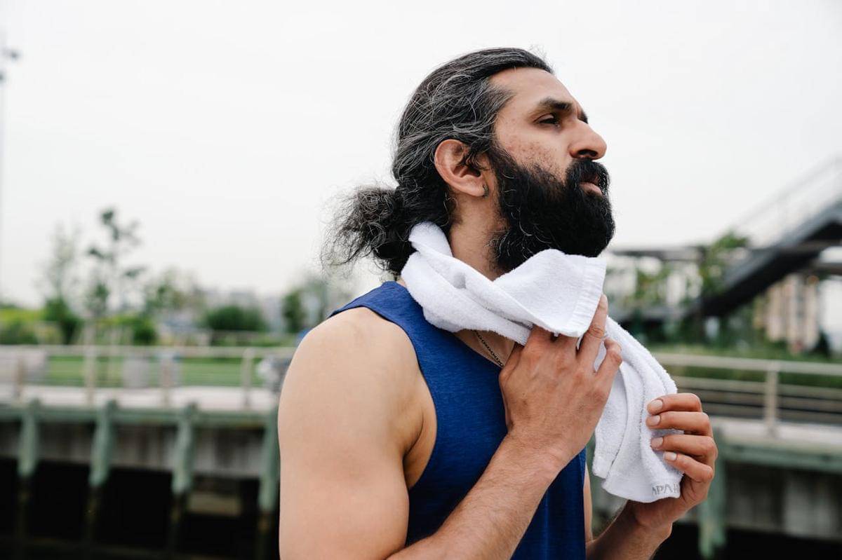 Seorang laki-laki sedang mengelap keringat di lehernya dengan handuk.