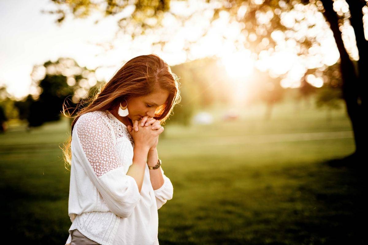 Seorang wanita sedang berdoa di sebuah ladang hijau (Unsplash/benwhitephotography)