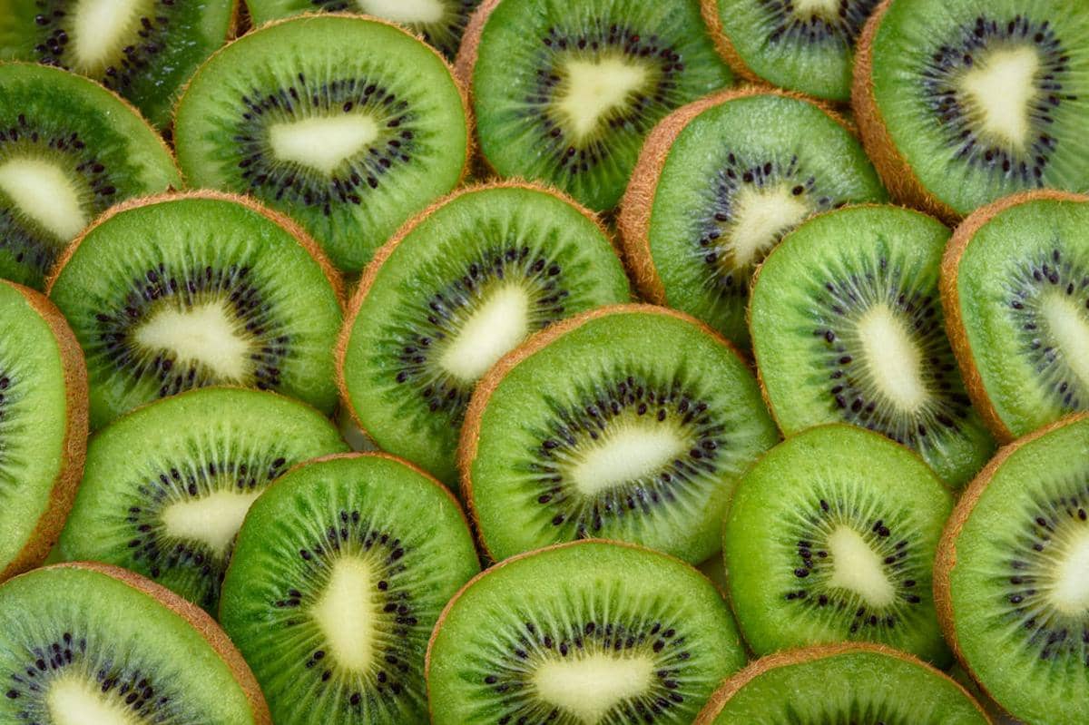 Irisan buah kiwi segar berwarna hijau dengan biji hitam kecil tersusun rapat menampilkan tekstur dan warna yang kontras.