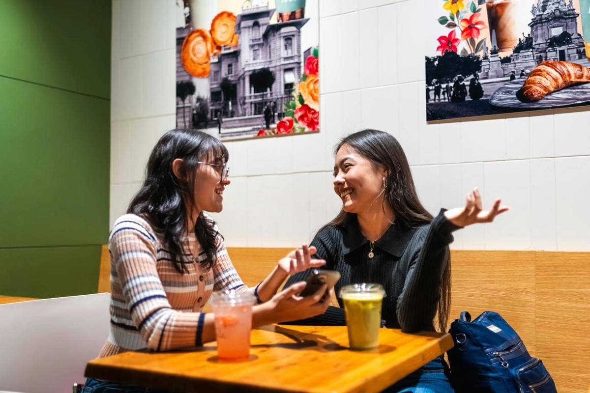 Dua wanita muda mengobrol di sebuah kafe dengan minuman di meja
