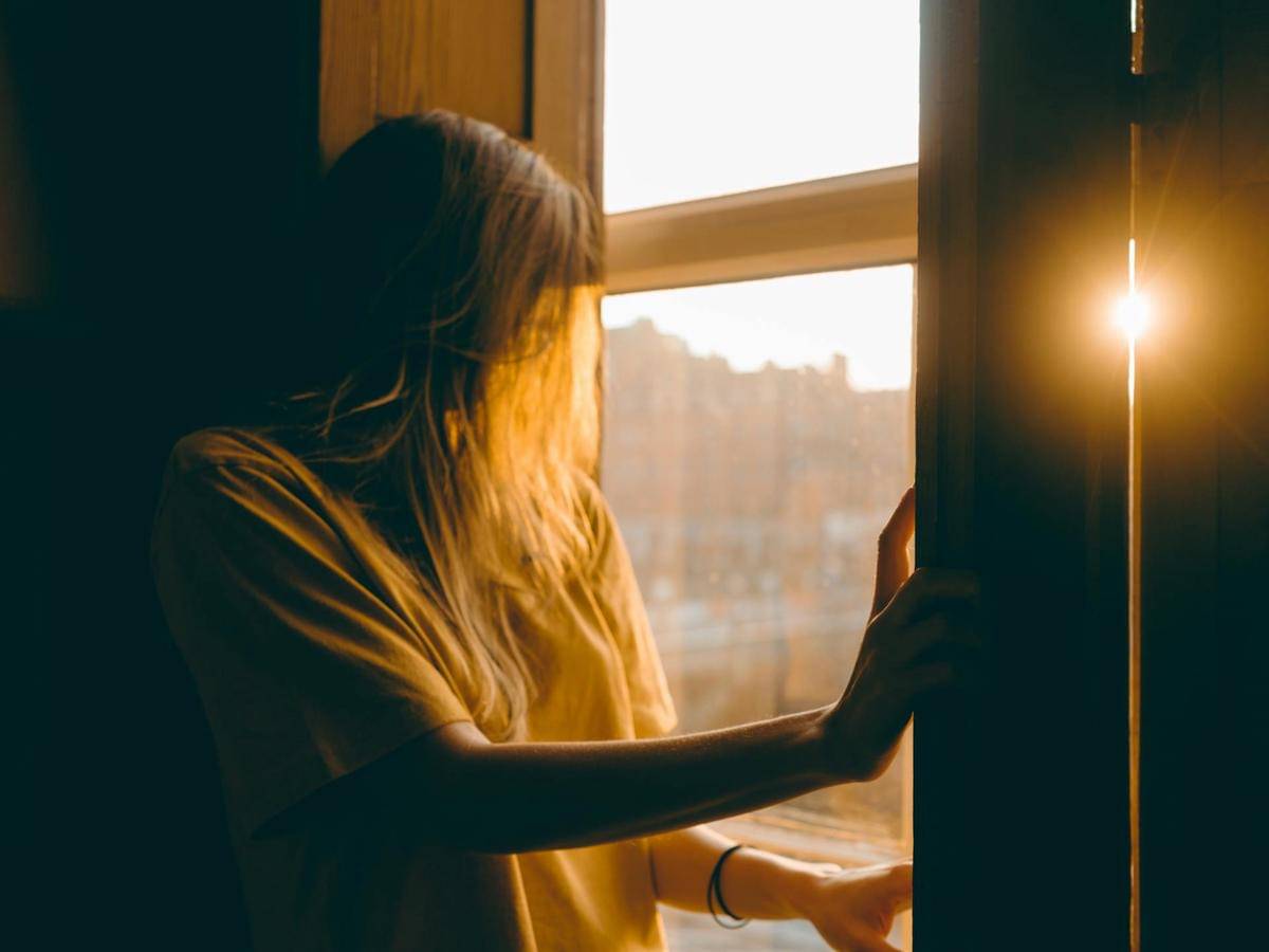 seorang wanita yang menatap jendela pada senja hari