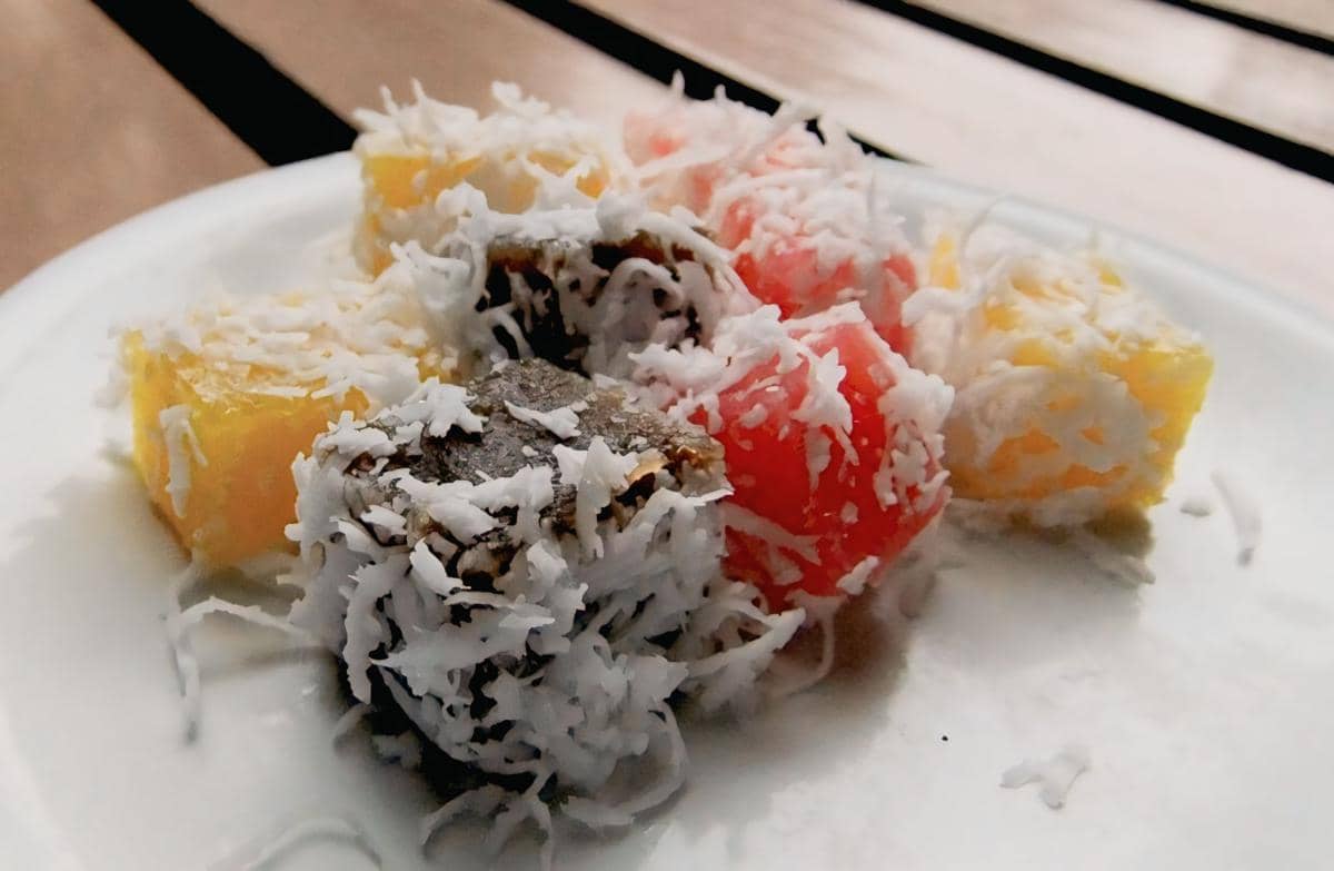 Beberapa potong cenil berwarna merah, kuning, dan hitam disajikan di atas piring putih, dilapisi parutan kelapa putih.