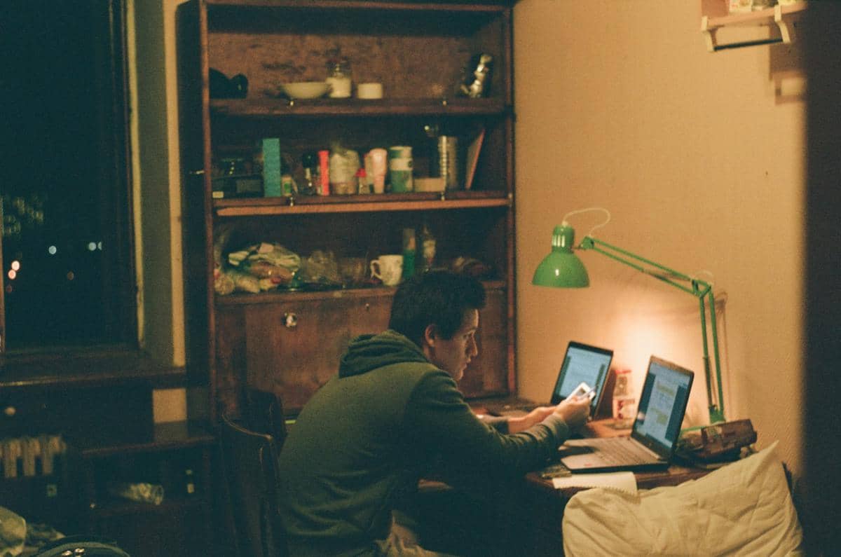 Anak kos bekerja di kamar menggunakan dua laptop