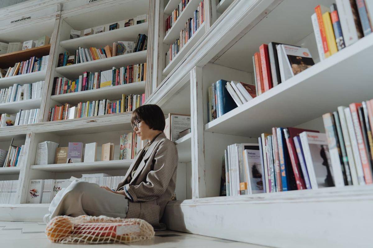 Seorang wanita duduk di bawah rak buku.
