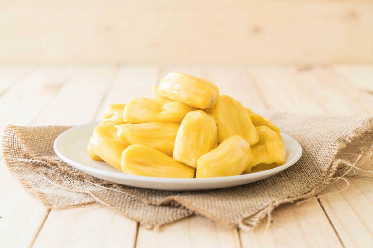 Potongan daging buah nangka matang berwarna kuning dengan tekstur berserat, tersusun rapat di atas permukaan putih.